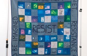A photograph of a blue patchwork quilt made during a workshop on Imagining Resistance.