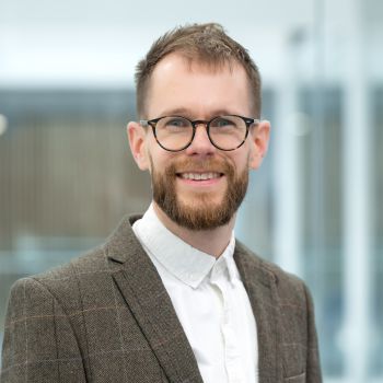 A professional portrait pic of Dr Dan Paget who wears glasses and a beard