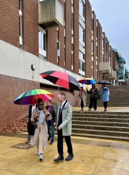 A group of people walking across the campus carrying colourful umbrellas