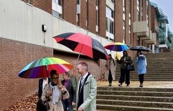 A group of people walking across the campus carrying colourful umbrellas