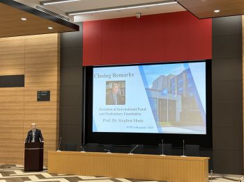 Prof Stehen Shute is shown speaking at a podium with a large screen behind him showing his name and title and 'Closing Remarks'