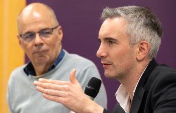 Professor David Ruebain looking at Luke Tryl speaking into a microphone