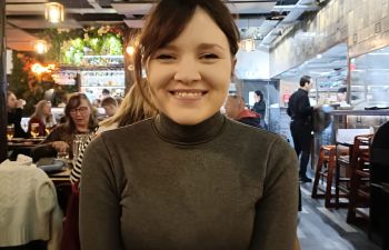 Coral Buckland, a dark haired lady smiling at the camera whilst seated in a restaurant