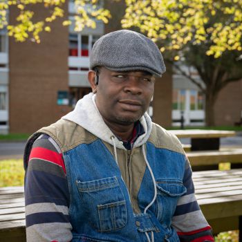 Michael Fadeyi sitting outside on a bench with a beautiful tree in the background.