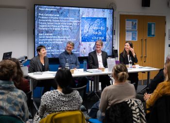 Two women and two men sat at a table facing the audience with a presentation screen behind them