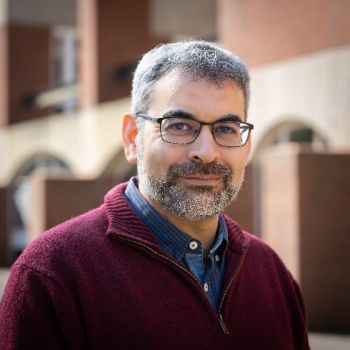 Professor Robin Banerjee, Pro-Vice-Chancellor (Global and Civic Engagement) smiling at the camera and standing in front of a red brick university building