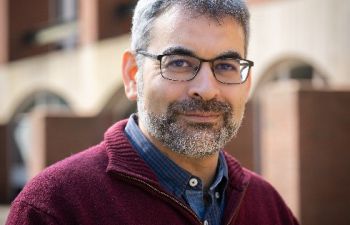 Professor Robin Banerjee, Pro-Vice-Chancellor (Global and Civic Engagement) smiling at the camera and standing in front of a red brick university building