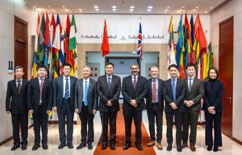 Group of 9 men and one woman at UIBE standing in front of international flags, smiling