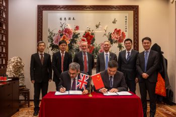 two men sat at table signing MOU with six men standing behind