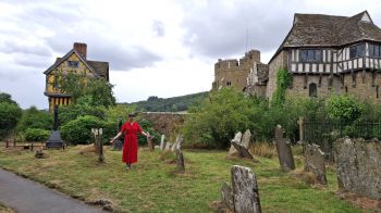 Alexandra Loske standing among old gravestones, with Stokesay Castle in Shropshire in the background