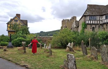 Alexandra Loske standing among old gravestones, with Stokesay Castle in Shropshire in the background