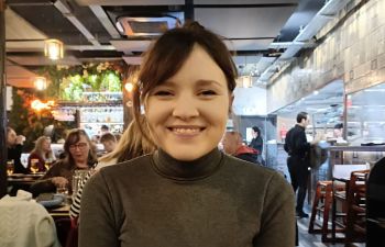 Coral Buckland seated at a table in a restaurant and smiling at the camera