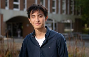 James Hews standing in front of a red brick university building and smiling at the camera