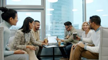 three men and three women sat in an office area talking and looking at a laptop.