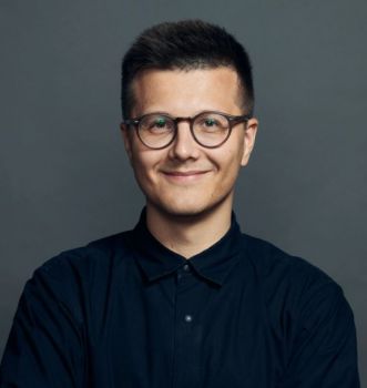 A smiling young man, with short dark hair, wearing glasses and a black top