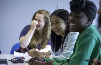 A photo of three women smiling and laughing in a University classroom setting