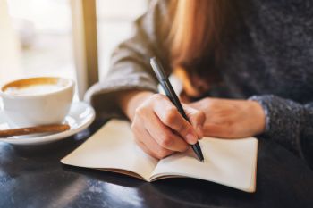 A person writing in a journal next to a a cup of coffee