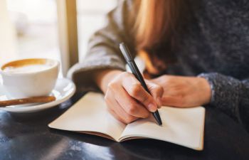 A person writing in a journal next to a a cup of coffee