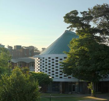 The Meeting House at the University of Sussex, a round white building with a green roof surrounded by trees