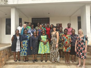 Around sixteen staff members stand together on steps outside a building at the University Of Ghana, they are smiling at the camera. The group is positioned in two rows in front of an entrance with pillars and open doors.