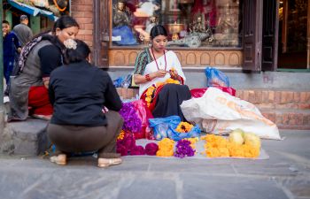 Newari woman in traditional attire crafting globe amaranth garlands, Patan Durbar Square, Lalitpur, Nepal