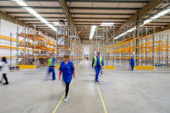 Workers in a large warehouse walk in different directions.