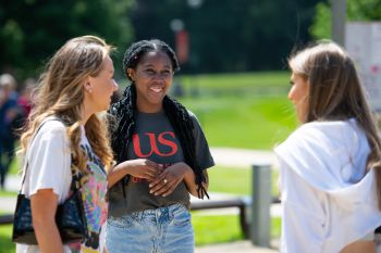 Smiling students talking on campus, one wears a University of Sussex t-shirt