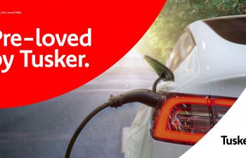 'pre loved cars' written in white on red semi-circle background in top right hand corner. Grey car in the remaining part of the image with 'Tusker' written in black on the bottom right corner.