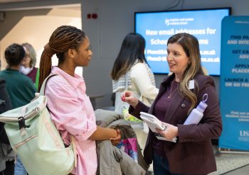 A student talking with an alumni speaker in front of a blue banner and screen