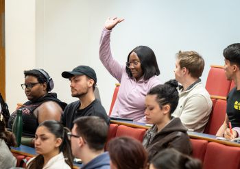 A group of students in a lecture theatre, one student with their hand up asking a question