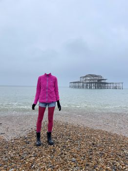Person standing on Brighton beach with the West pier behind them. The person's head has been removed from the photo.