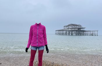 Person standing on Brighton beach with the West pier behind them. The person's head has been removed from the photo.