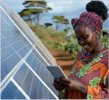 A lady in a colorful dress stood next to solar panels reviews readings on a tablet