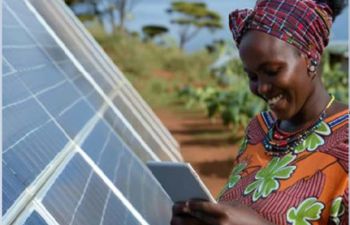 A lady in a colorful dress stood next to solar panels reviews readings on a tablet