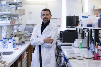 Professor Georgios Giamas wearing a white lab coat in a science laboratory in the University of Sussex. He is smiling and has his arms crossed.