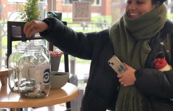 A photo of someone voting for a charity but placing coffee beans in a jar