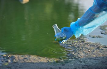 Close-up environmentalist hand of a researcher in a process of taking a sample of contaminated water from a lake