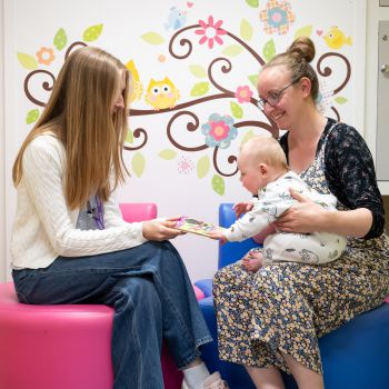 A baby sitting on a caregiver's lap reaches for a picture book