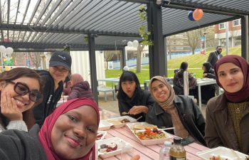 Six women smile around a table with food