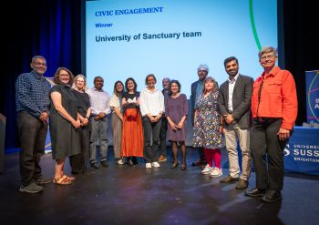 A photograph of 12 members of the University of Sanctuary team on stage at the awards ceremony with the VC, Prof Sasha Roseneil, stood at the far right of the group.