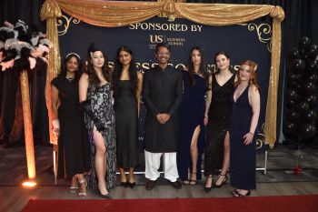 Students and faculty member dressed in formal party wear standing before a decorated display board