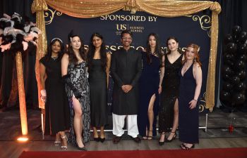 Students and faculty member dressed in formal party wear standing before a decorated display board