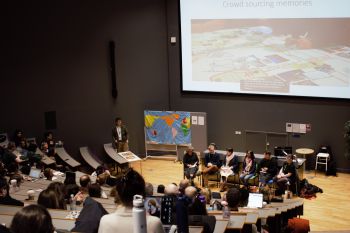 A panel of speakers sit in front of a map and a large screen with a presentation slide on it entitled 'Crowd sourcing memories'.