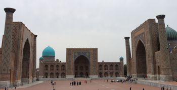 This photograph shows the structures surrounding 3 sides of an impressively large square in Uzbekistan. Each side features an enormous doorway. Ceiling domes are also visible behind these.