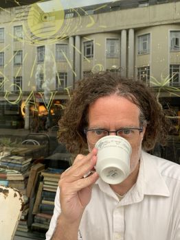 Man with blonde hair and a mug covering his face