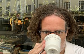 Man with blonde hair and a mug covering his face