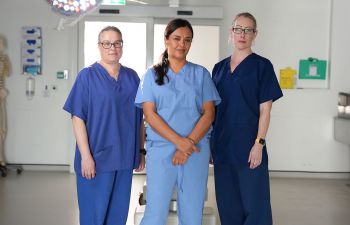 A photo of Prof Jeanette Rotchell (Lincoln), Liz Bonnin and Prof Claire Smith (BSMS) in blue scrubs in the BSMS dissection rooms on the Sussex campus
