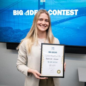 Image of Jacqueline holding up a certificate in front of a 'Big Ideas Contest' blue screen