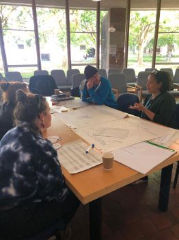 Participants taking part in a group discussion. People are seated around a table covered with flipchart paper and workshop materials.