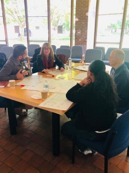 Participants taking part in breakout session. People seated around a table discussing action plan priorities and reviewing workshop materials.